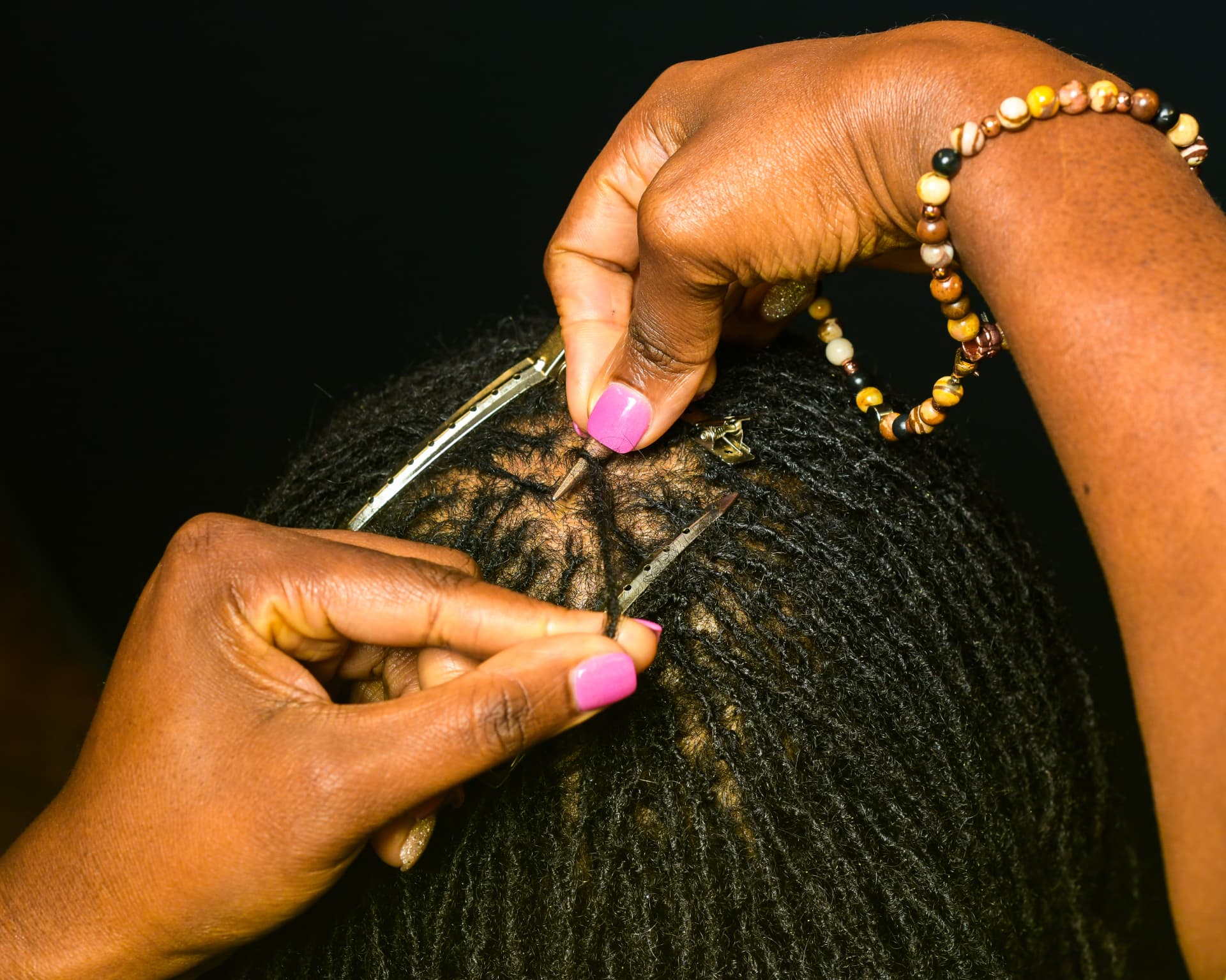 Hands working with precision on a client’s locs using the Signature Loc Method